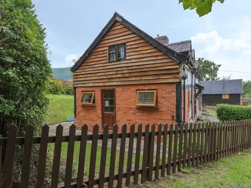 Caerau Farm House, a brick and timber-clad cottage with a picket-fenced garden