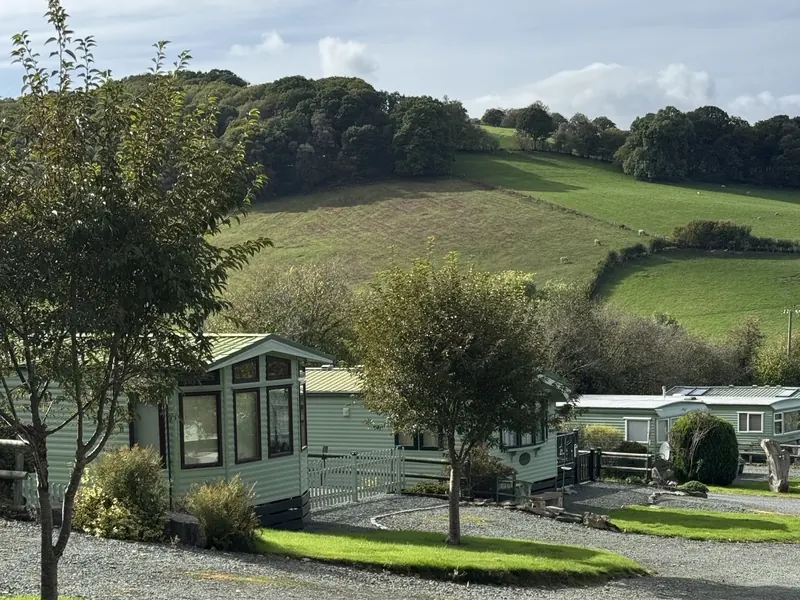 Holiday homes set among trees and lawns at Caerau Park, with green hillsides behind
